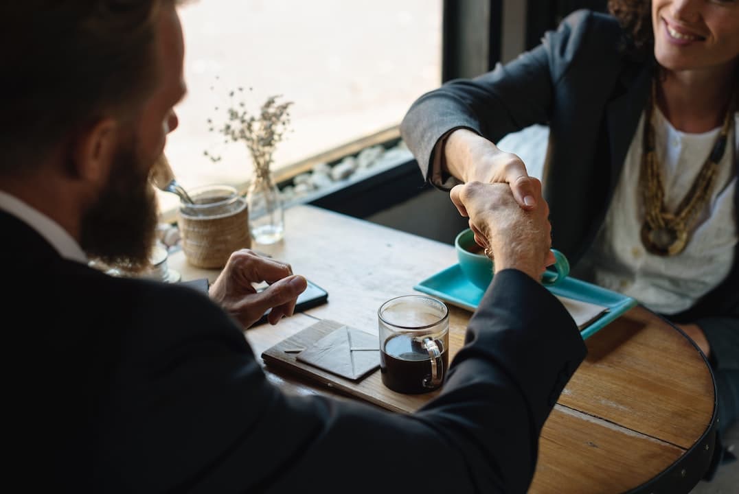 adults shaking hands over table
